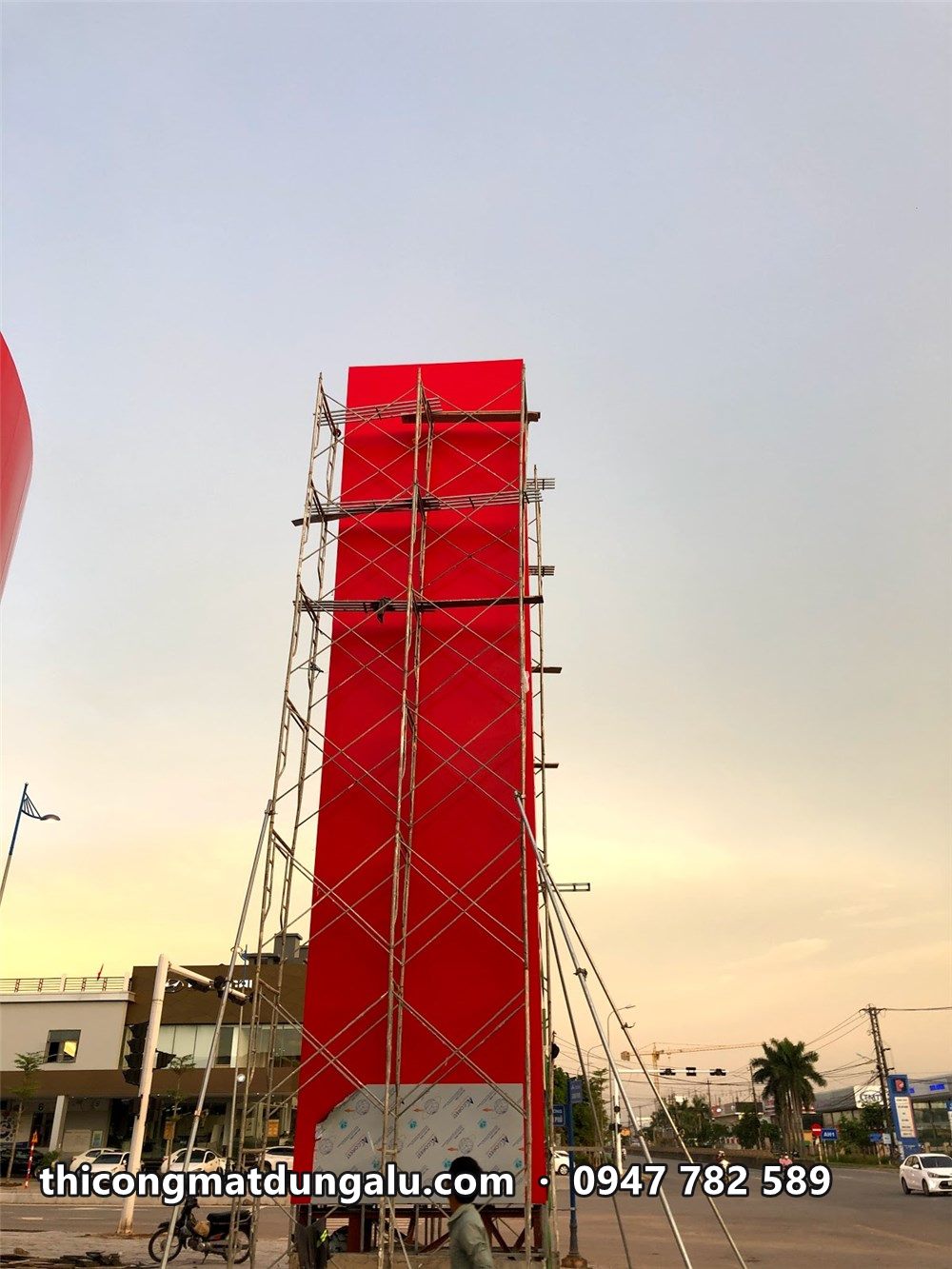 Trụ pylon đỏ phủ kín alu, giàn giáo còn bao quanh, trời hoàng hôn