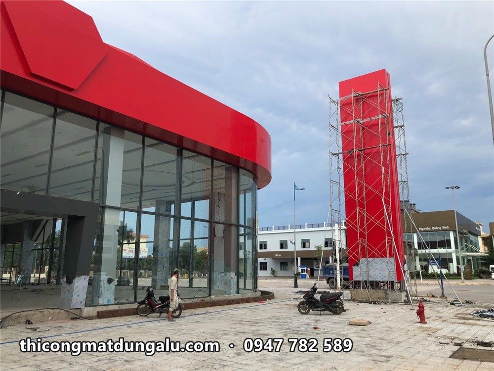 Trụ pylon đỏ hoàn thiện đứng cạnh showroom mặt kính có dải mái cong đỏ