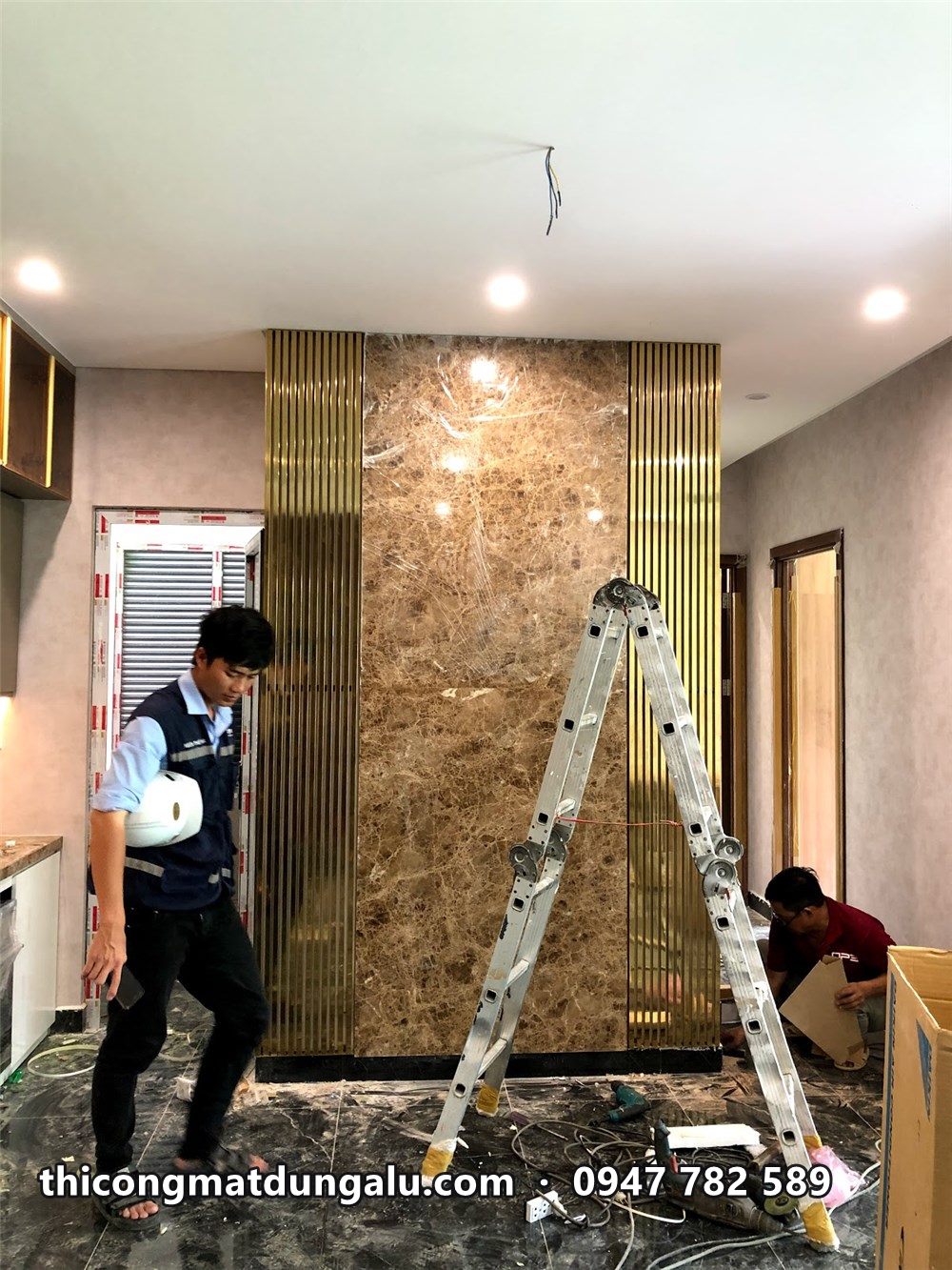 Thợ lắp thanh inox vàng cạnh vách đá ở lối vào căn hộ mẫu