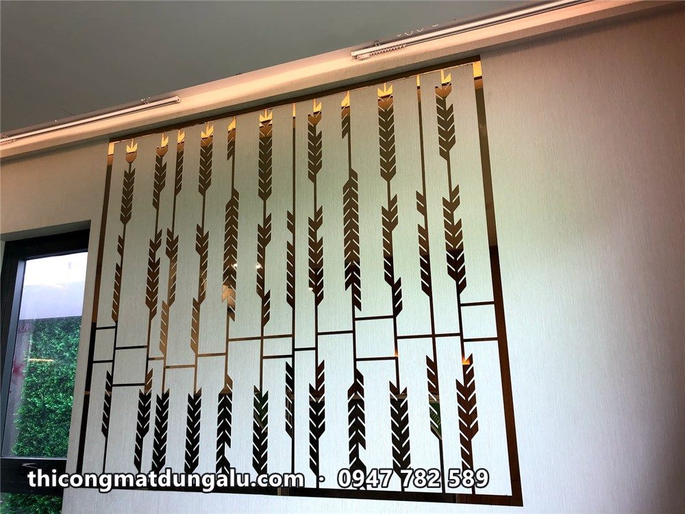 Vách inox bông lúa vàng hoàn thiện trên tường trắng có đèn rọi